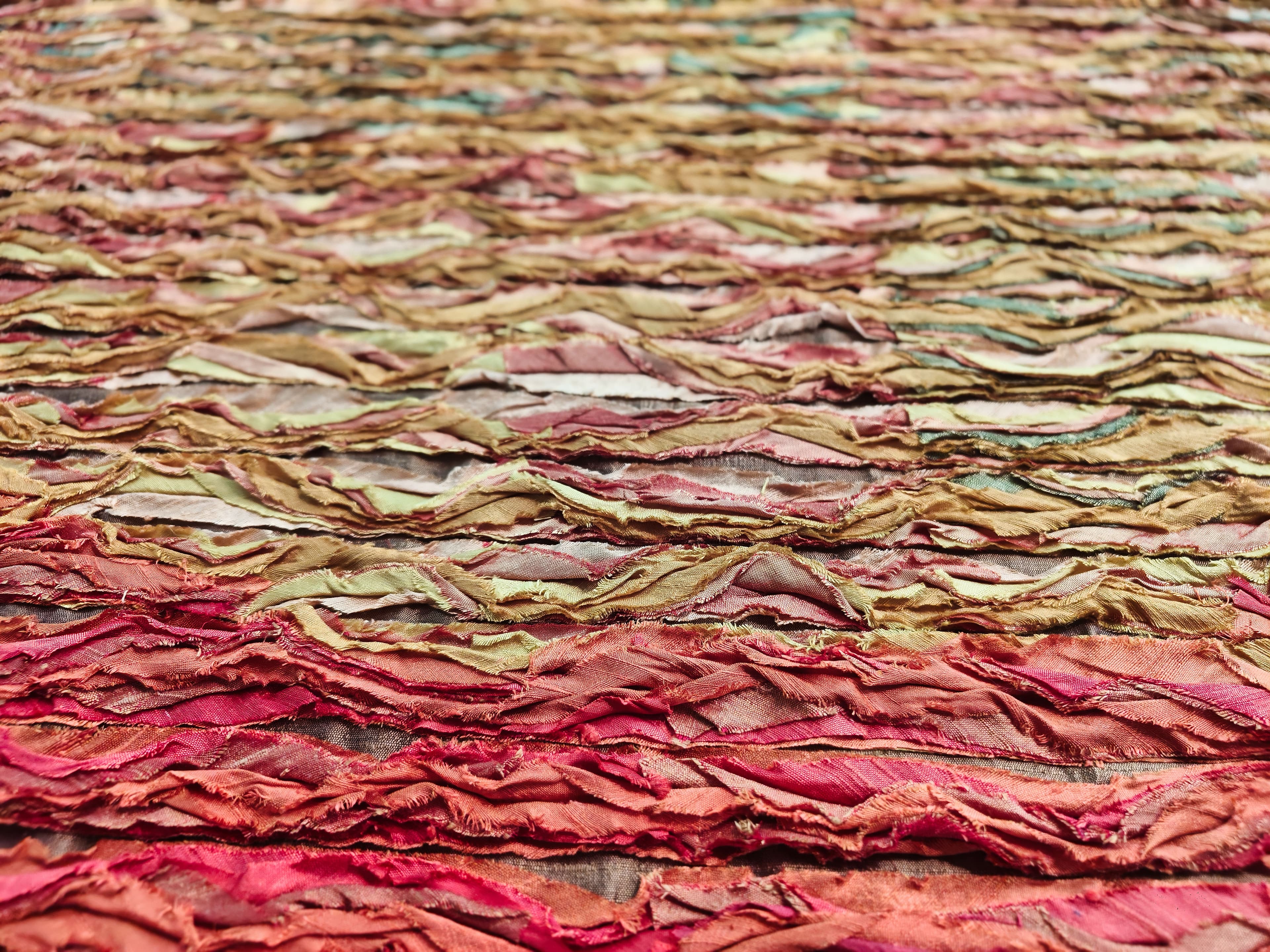 Colourful abstract textile art featuring layered and textured fabric swatches in warm tones.